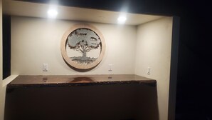 Quarto com uma mesa de madeira, uma obra de arte de uma árvore na parede e duas tomadas.