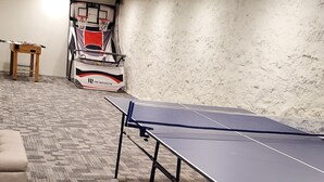 Mesa de pingue-pongue, aros de basquete e um sofá numa sala com carpete estampado.