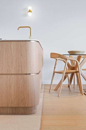 A modern kitchen with a wooden countertop, a gold faucet, and a table with chairs. - Drift by Coast Hosting (Avoca Beach)