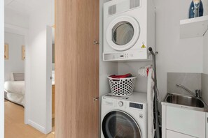 A compact laundry area with a washing machine, dryer, and a small sink. - Avoca Lake View Luxury Apartment (Avoca Beach)