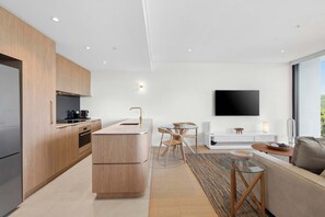 A modern kitchen with wooden cabinets, a central island, and a dining area with a table and chairs. - Drift by Coast Hosting (Avoca Beach)