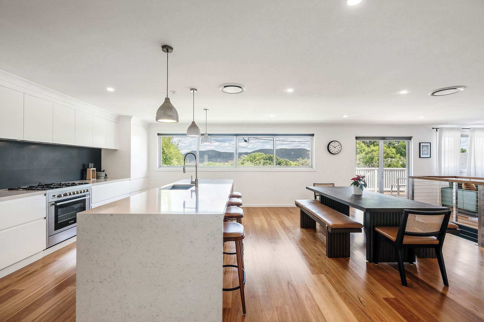 A modern kitchen with a large island, wooden flooring, and a view of the outdoors.