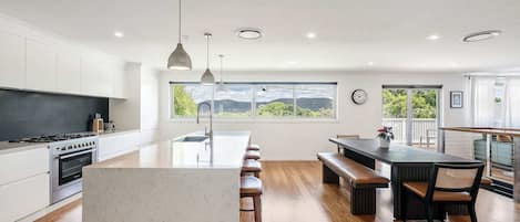 A modern kitchen with a large island, wooden flooring, and a view of the outdoors.