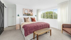 Une chambre à coucher avec un lit, un banc, une fenêtre avec des rideaux et une porte.