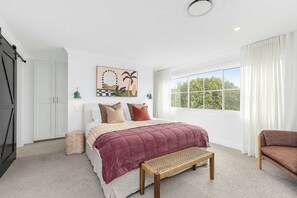 Ein Schlafzimmer mit einem Bett, einer Bank, einem Fenster mit Vorhängen und einer Tür.