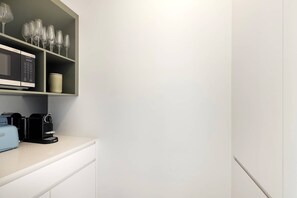 A kitchenette with a microwave, coffee maker, and wine glasses on a shelf. - The Oasis by Coast Hosting (Umina Beach)