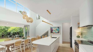 Une cuisine moderne dotée d’un grand îlot central, de meubles blancs et d’un coin repas avec des chaises en osier.