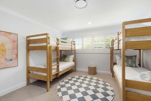 Ein Zimmer mit zwei Etagenbetten, einem runden Teppich, einem kleinen Holzschemel und einem Fenster mit Jalousien.
