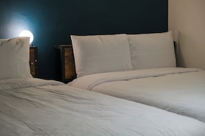 Two beds with white bedding, wooden headboards, and a wall-mounted light.