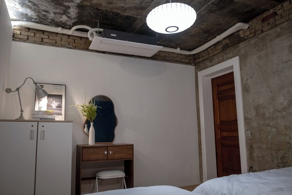 Ein Zimmer mit einem Bett, einem Schreibtisch mit Stuhl, einem Kleiderschrank, einem Spiegel und einer Tür.