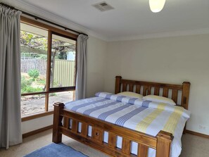 Un dormitorio con cama de madera, ventana con cortinas y vistas al exterior.