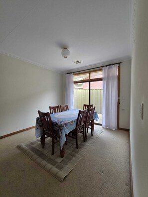 Comedor con una mesa dispuesta para seis personas, una ventana con cortinas e iluminación en el techo.