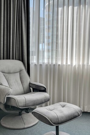 A modern chair with a footrest, a round base, and a window with sheer curtains. - Stylish CBD Apartment w/ Pool & Gym Access (Brisbane City)