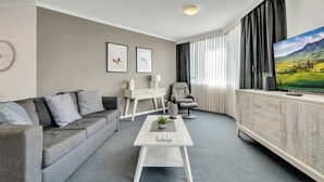 Un soggiorno moderno con un divano grigio, un tavolino da caffè bianco, una TV su un mobile in legno e un quadro di un paesaggio.