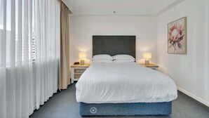 Camera d'albergo con un letto grande, due comodini con lampade, una finestra con tende leggere e un'opera d'arte appesa al muro.