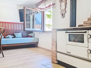 Una habitación acogedora con piso de madera, un sofá con cojines, una ventana con vistas y una estufa blanca.