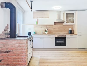 Una cocina con estufa de ladrillo, armarios blancos, encimera de madera y horno empotrado.