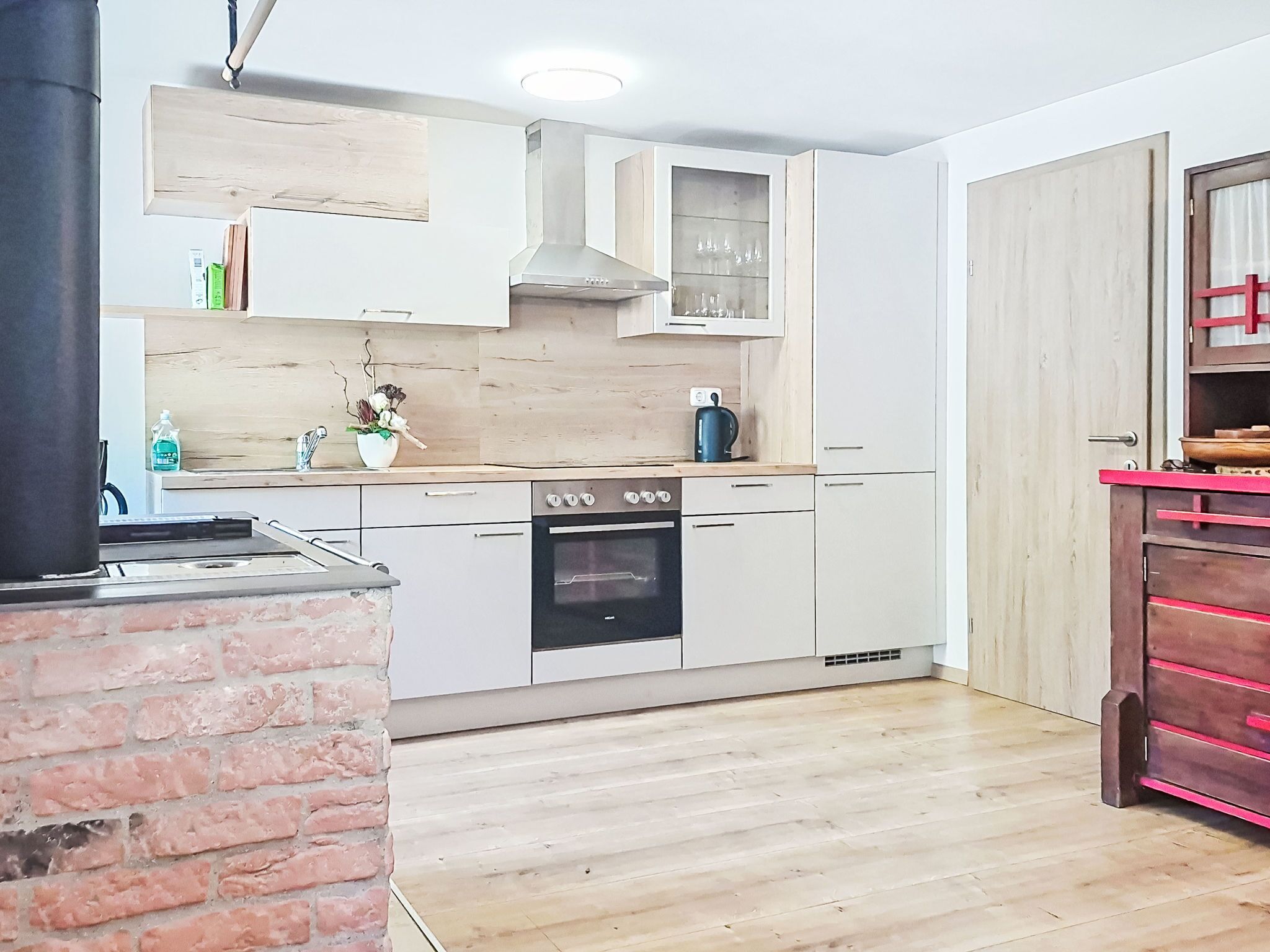 A kitchen with a brick wall, white cabinets, a stove, and a coffee machine.