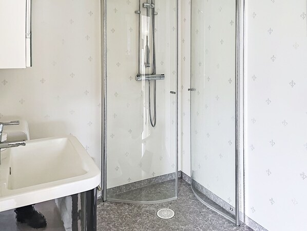 A bathroom with a glass-enclosed shower, a white sink, and patterned wallpaper.
