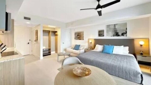 Een moderne hotelkamer met een bed, een eettafel, een plafondventilator en uitzicht op de stad.