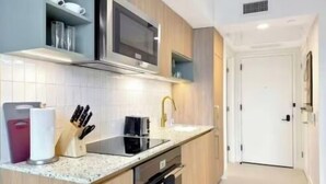 Een kleine keuken, voorzien van een magnetron, oven, spoelbak en moderne kastjes.