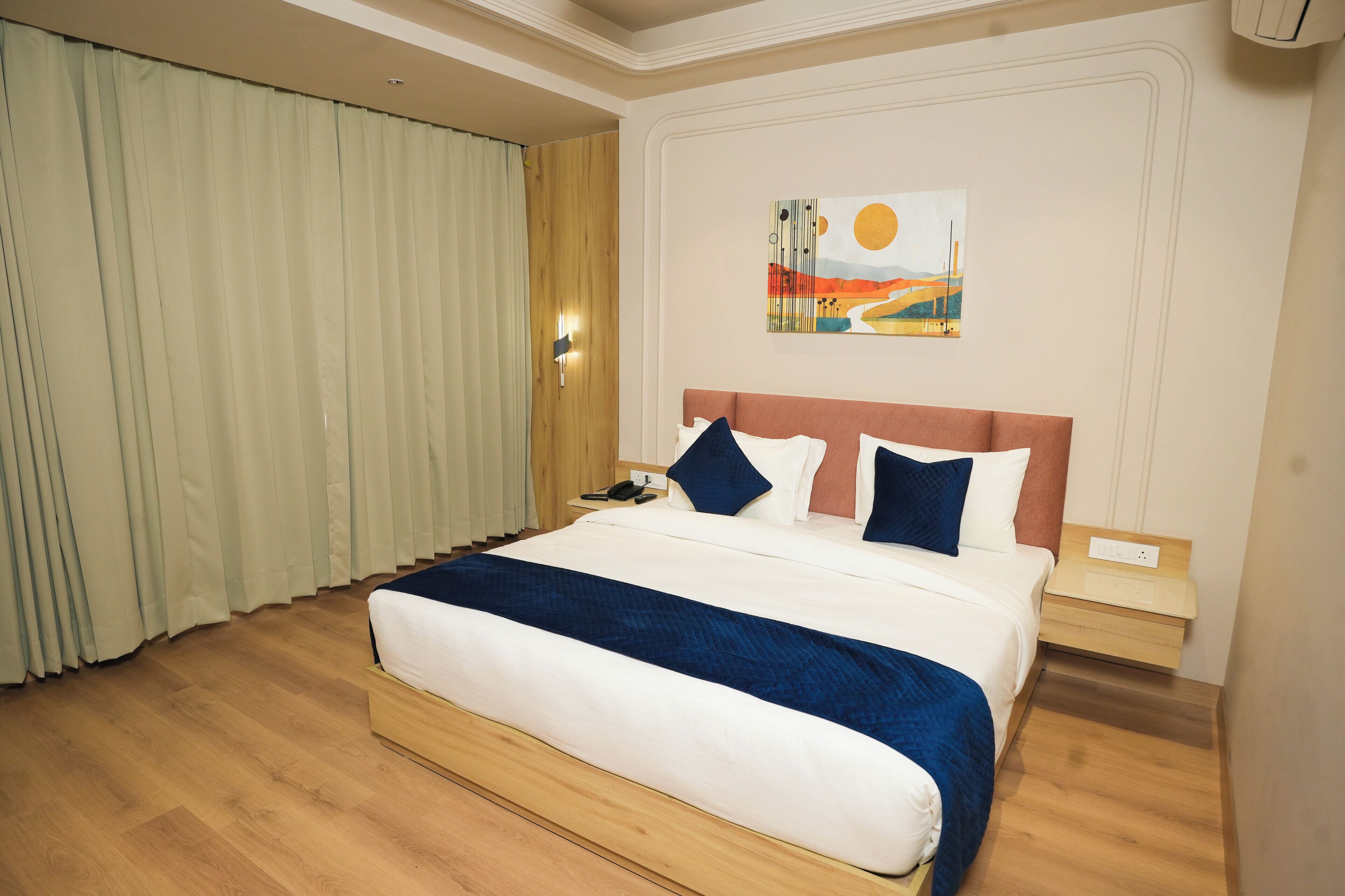 A hotel room with a large bed, a nightstand, a painting on the wall, and a window with curtains.