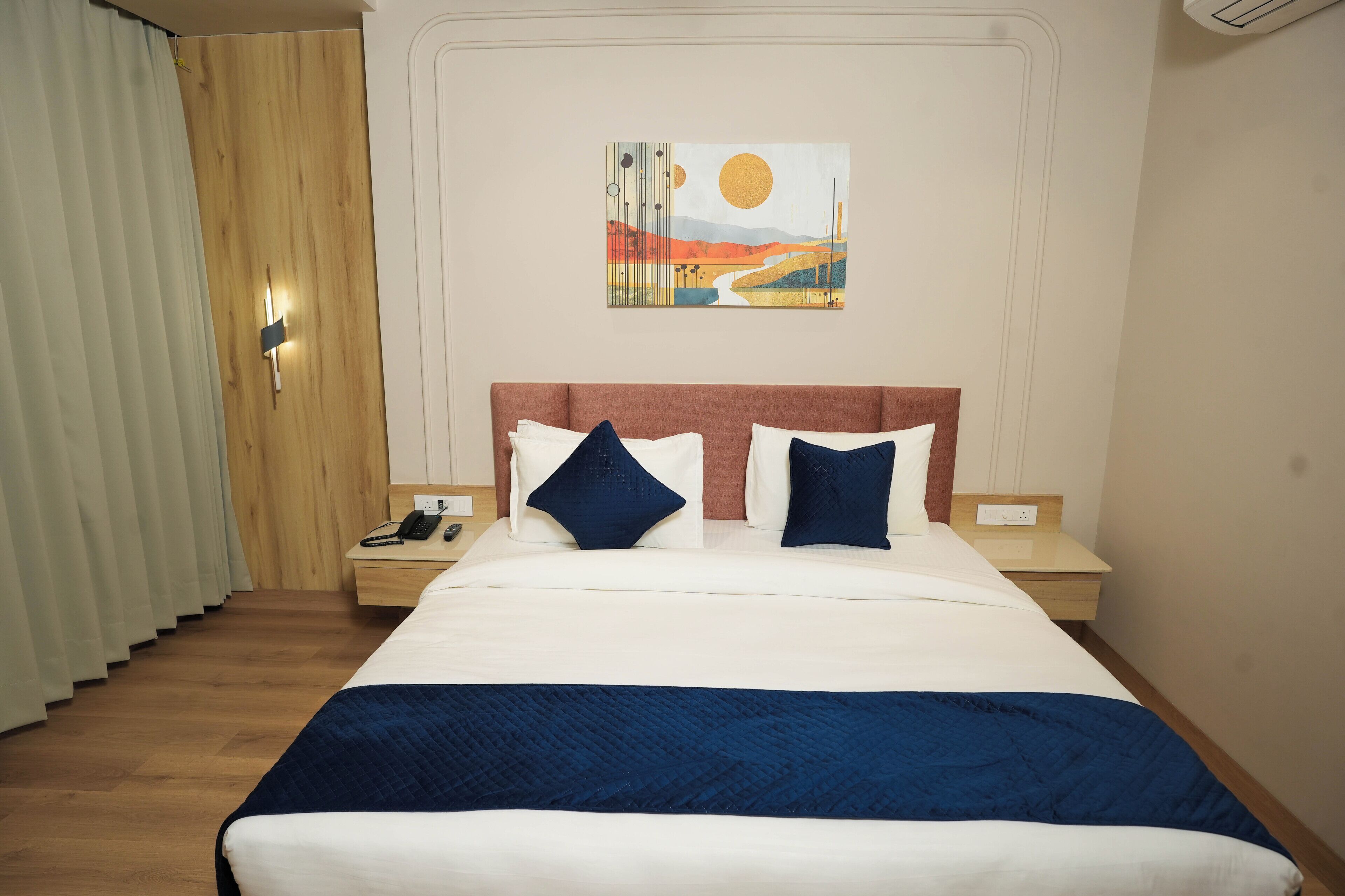 A hotel room with a large bed, a nightstand, a telephone, a painting on the wall, and a wooden door.