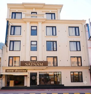 Ett hotell med flera våningar, med en skylt som visar texten ”HOTEL SATNAM” och en tydligt markerad entré.