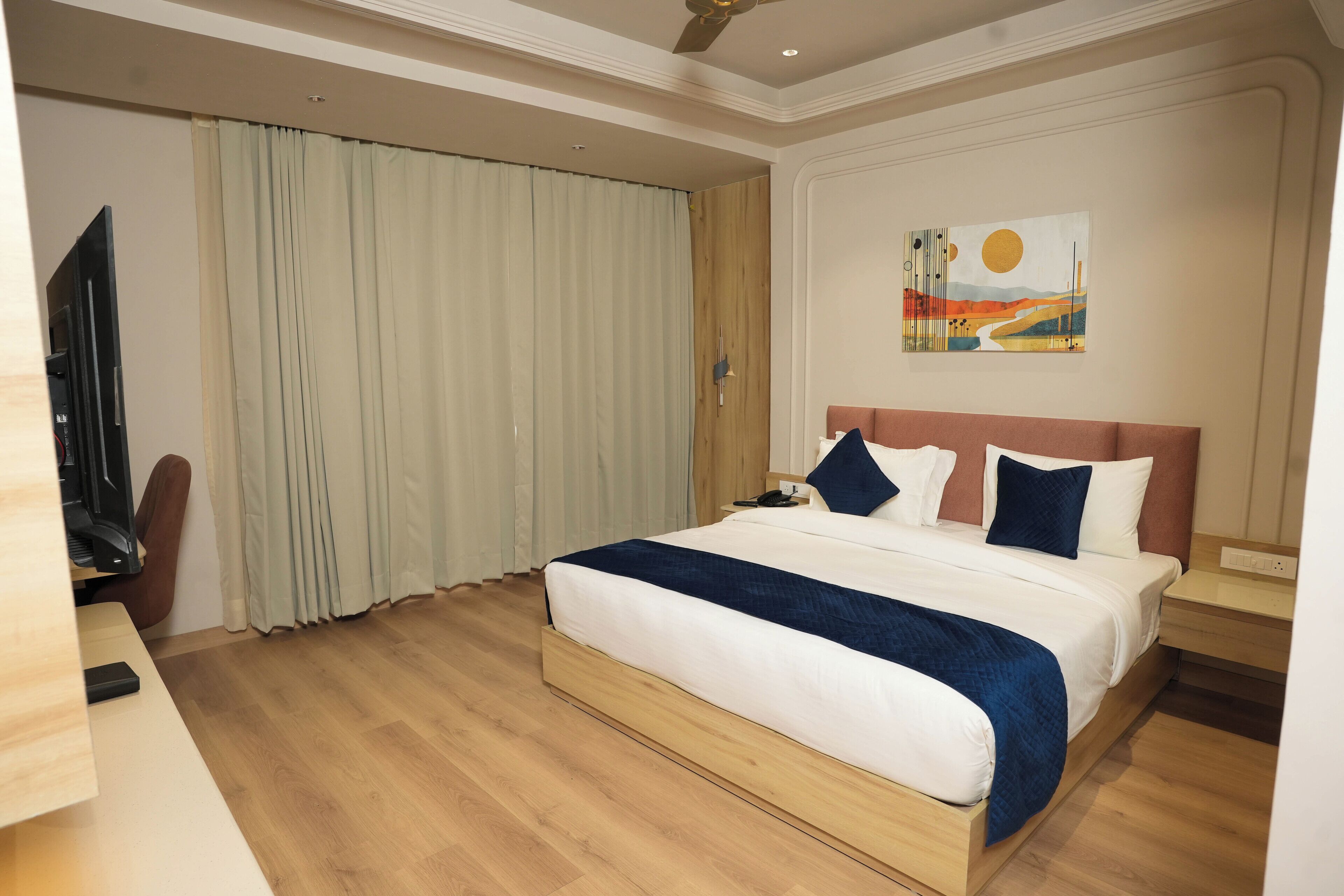 A hotel room with a bed, a desk, a television, and a painting on the wall.