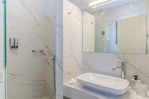 Un baño moderno con un lavamanos blanco, cabina de ducha de vidrio y paredes de mármol.