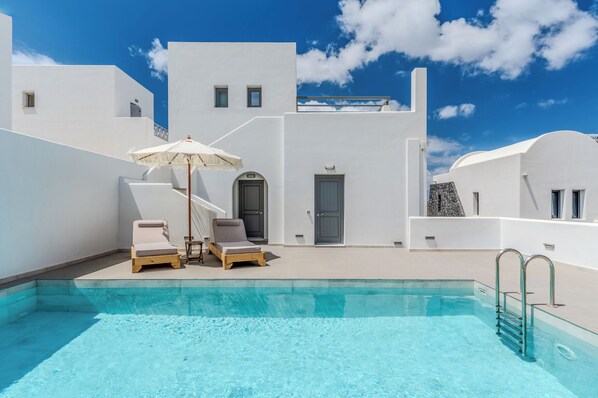 A pool area with lounge chairs and a door, surrounded by white buildings under a clear sky. - Soma Wellness & Spa Concept (Santorini)