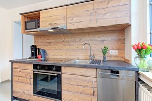 Eine moderne Küche mit Holzausstattung, einer integrierten Mikrowelle, einer Kaffeemaschine, einem Spülbecken und einem Geschirrspüler.