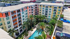 A multi-story hotel with balconies, a swimming pool, and a parking area. - Moorings Pool Overview Resort (Lantana)