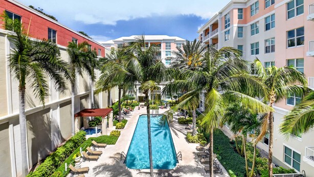 A pool surrounded by palm trees and buildings with balconies. - Moorings Pool Overview Resort (Lantana)