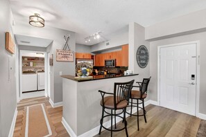A modern kitchen with a central island, bar stools, and a hanging light fixture. - Moorings Pool Overview Resort (Lantana)