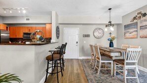 A modern kitchen with wooden cabinets, a dining area with a wooden table and chairs, and a clock on the wall. - Moorings Pool Overview Resort (Lantana)