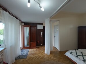 Ein Zimmer mit Bett, Holzboden, einer Tür und einem mit Vorhängen versehenen Fenster.