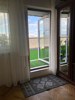 Una habitación con puerta de vidrio corredera que da a un balcón con césped y vistas a edificios.