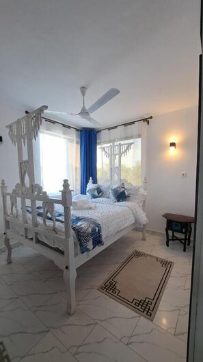 Ein Schlafzimmer mit Himmelbett, Deckenventilator, Nachttisch und Wandleuchte.