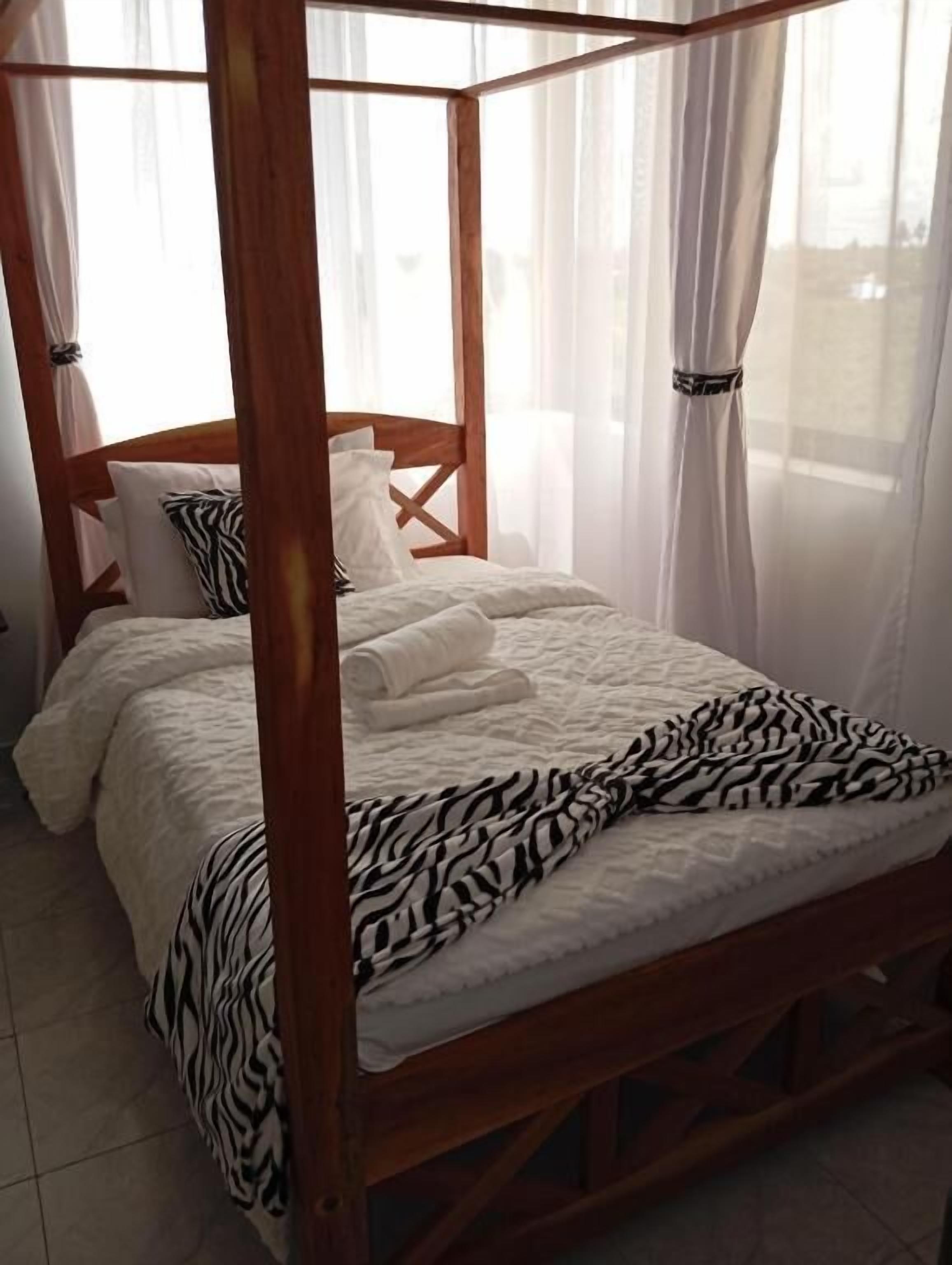 Ein Bett mit Baldachin, eine Decke mit Zeprazmuster, weiße Kissen und leichte Vorhänge.
