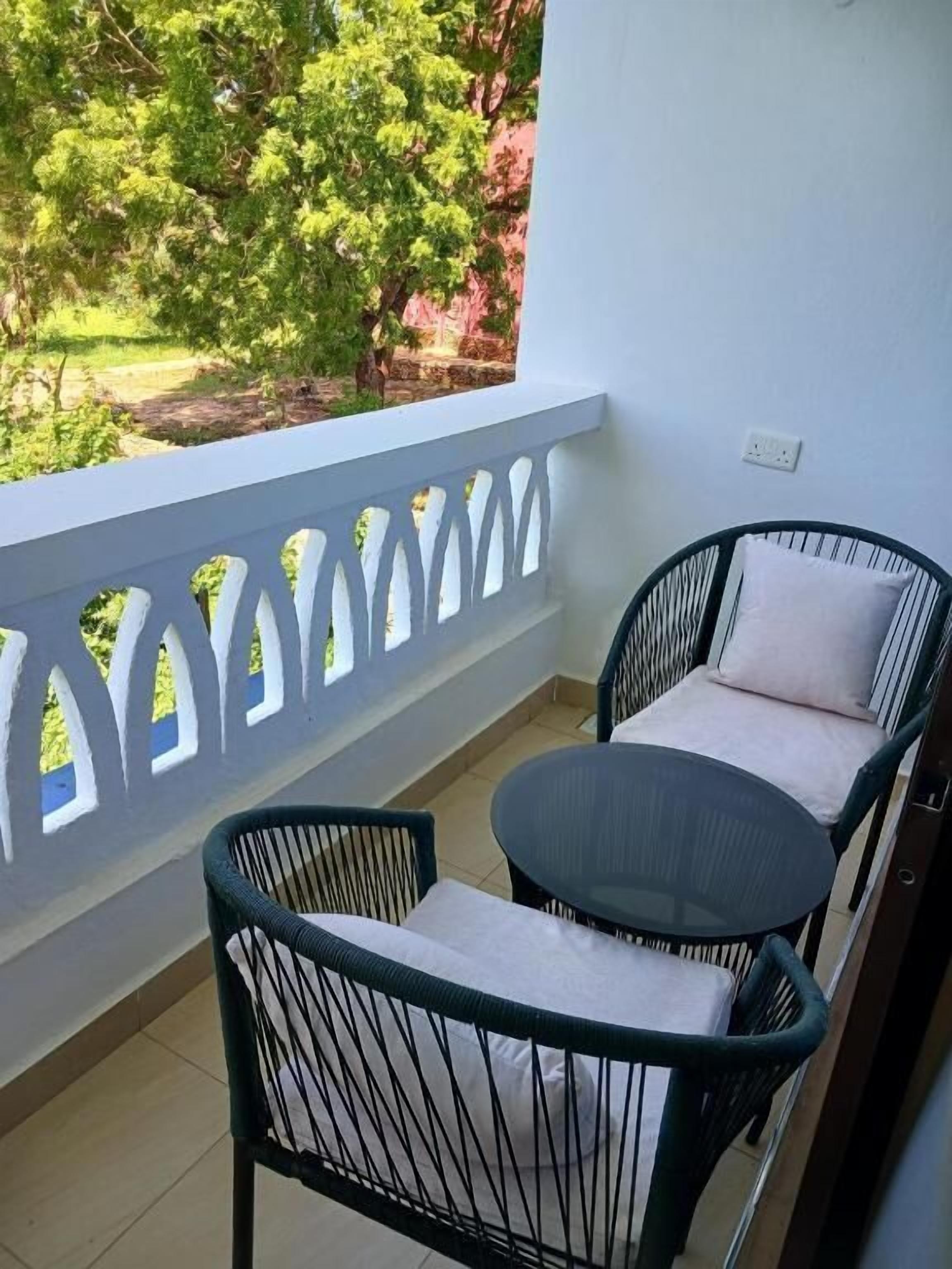 A balcony with a white railing, two black chairs with cushions, and a small round table.