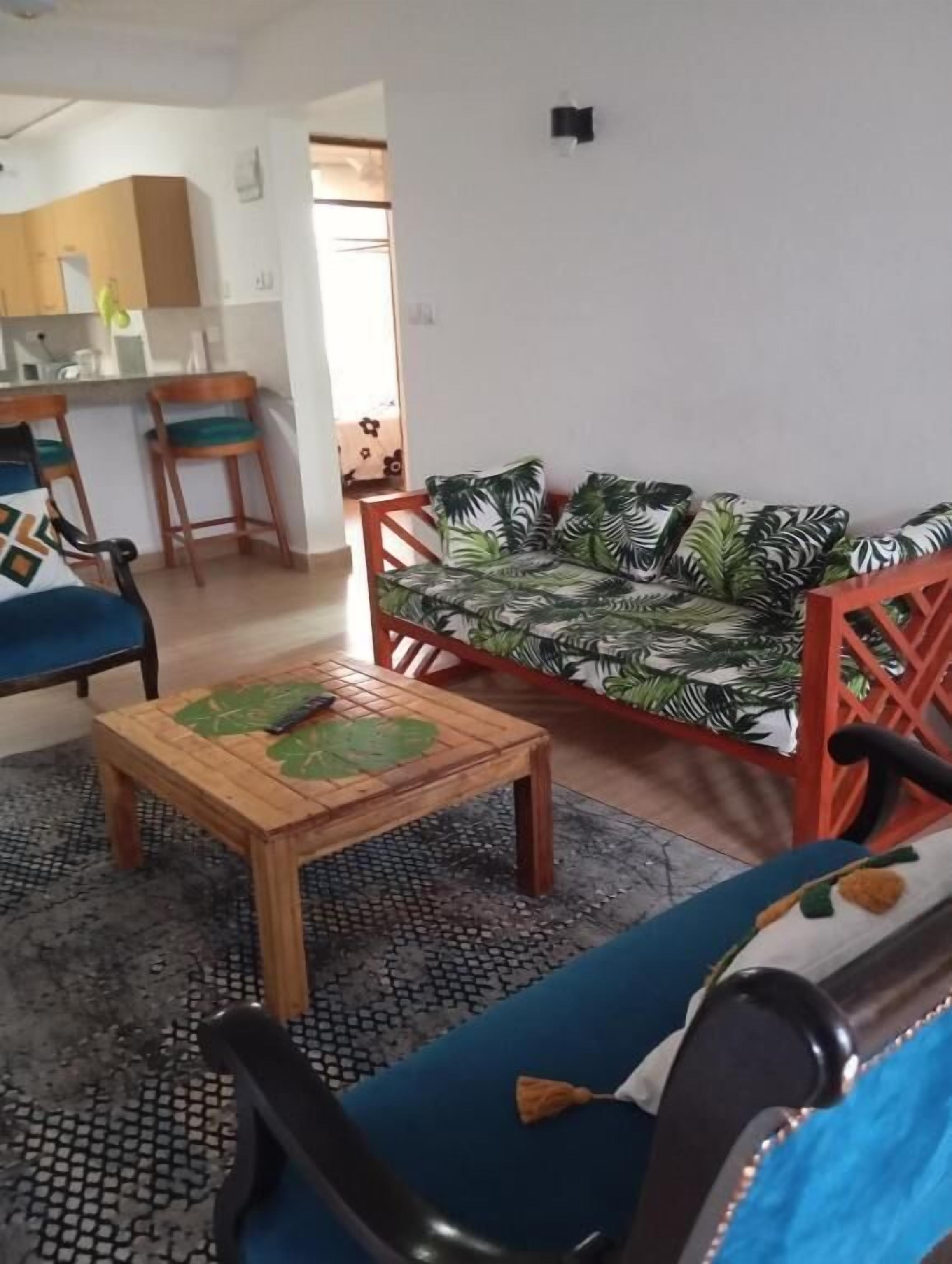 Un salon avec un canapé, des fauteuils, une table basse et, au fond, un coin cuisine.
