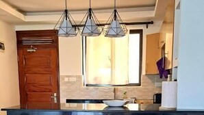 Una cocina con una isla central, dos taburetes de madera y luminarias colgantes.