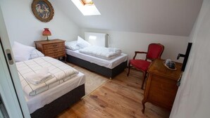 A bedroom with two beds, a wooden dresser, a red chair, a desk, and a skylight.