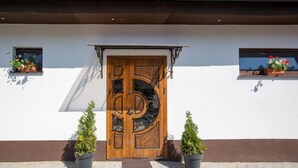 A building with a large wooden door, two potted plants, and a window with flowers.