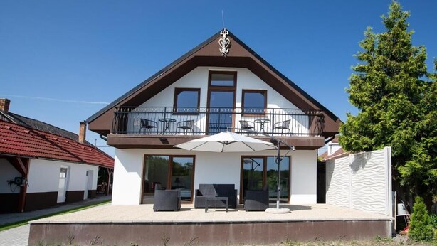A two-story house with a balcony, large windows, and outdoor seating.