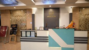 Taulell de recepció d'hotel amb un fons de paret de marbre, un senyal que diu 'PORTICO' i una estàtua decorativa.