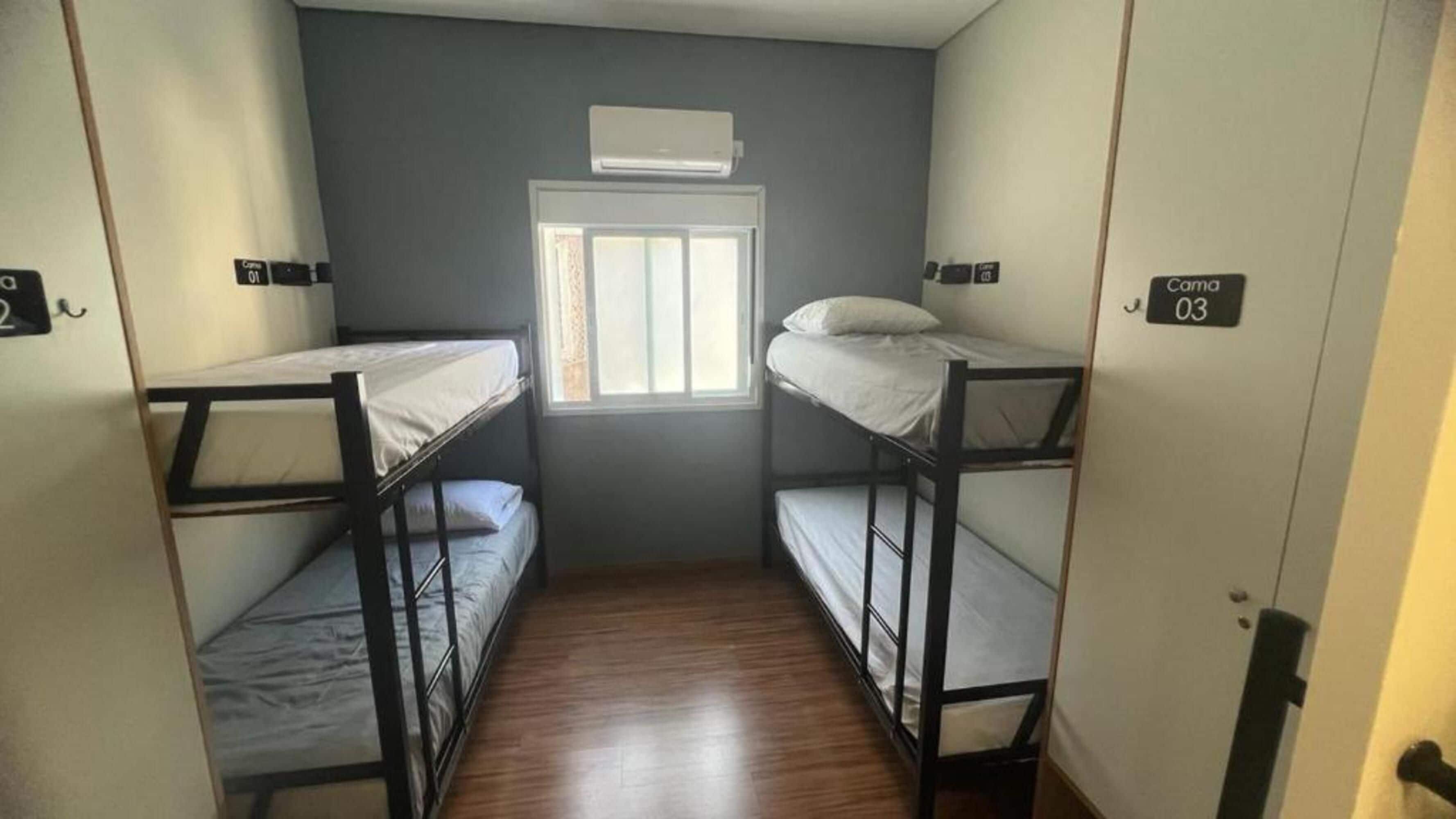 Une chambre avec deux lits superposés, une fenêtre avec des stores et un appareil de climatisation placé au-dessus de la fenêtre.