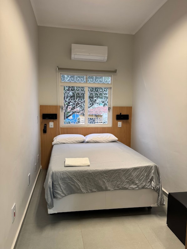 Habitación de hotel con cama, ventana de cristal decorativo, unidad de aire acondicionado y mesita de noche.
