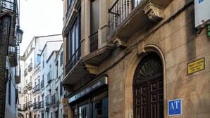 A street view with a building featuring a dark brown door, a blue sign with 'AT' on it, and a sign above the door indicating 'Pharmacy Calvo.'